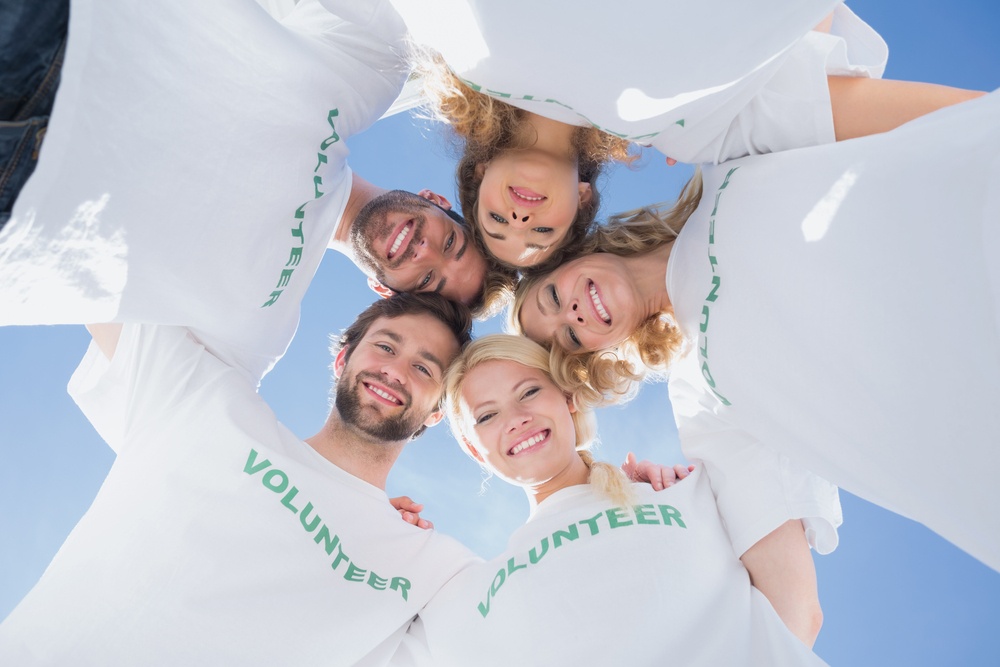 happy-volunteers-forming-a-huddle-against-blue-sky